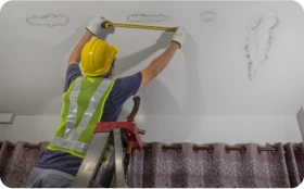 Trabajador con casco y chaleco midiendo una pared interior como parte de tareas de limpieza de tejados y mantenimiento.