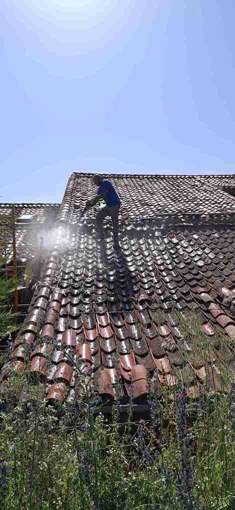 Trabajador limpiando tejado con agua a presión bajo el sol en Segovia