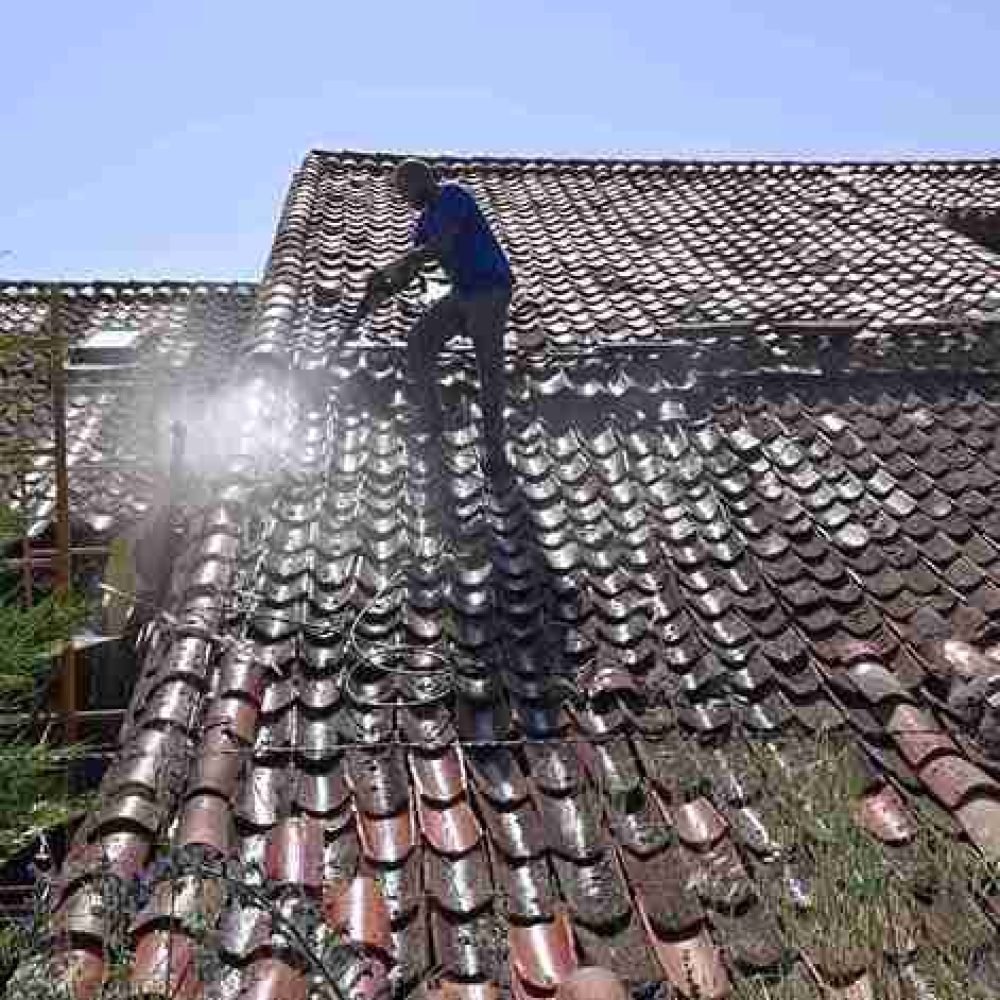 Trabajador limpiando tejado con agua a presión bajo el sol en Segovia