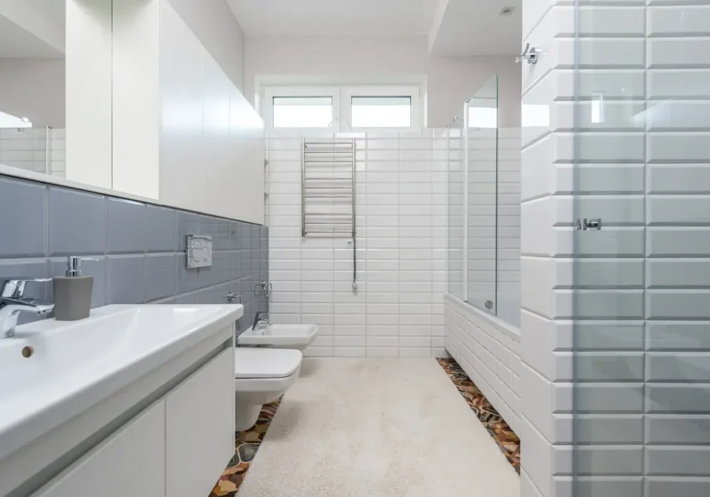 Inicio 11 Baño moderno con azulejos blancos y grises, lavabo doble y ducha con mampara en Segovia